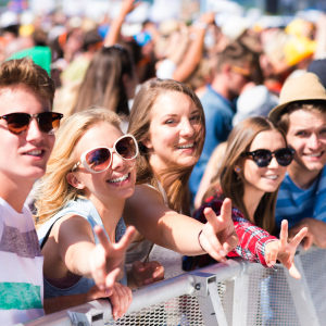 Teenagers at summer music festival under the stage in a crowd enjoying themselves, showing peace sign